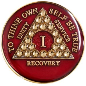 A red and gold sobriety chip with the letter i.