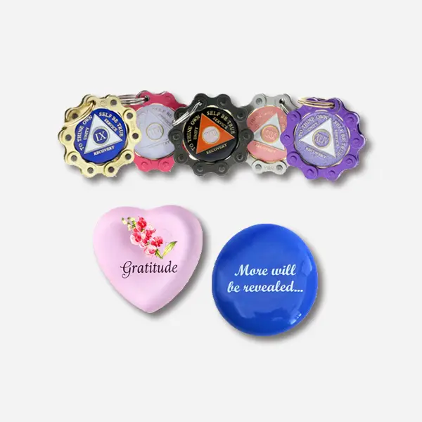A collection of unique recovery gifts featuring a Bike Chain Medallion Holder, a Language of Flowers Heart with a Sweet Pea representing "Gratitude", and a More Will Be Revealed Stone in Blue/White.